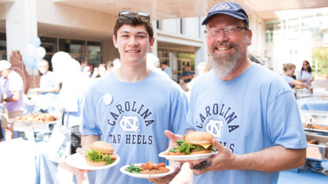 Father and son together, holding plates of food outside during Family Weekend.