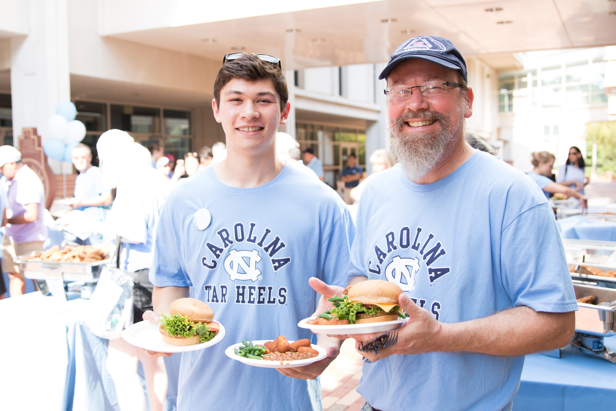 Father and son together, holding plates of food outside during Family Weekend.